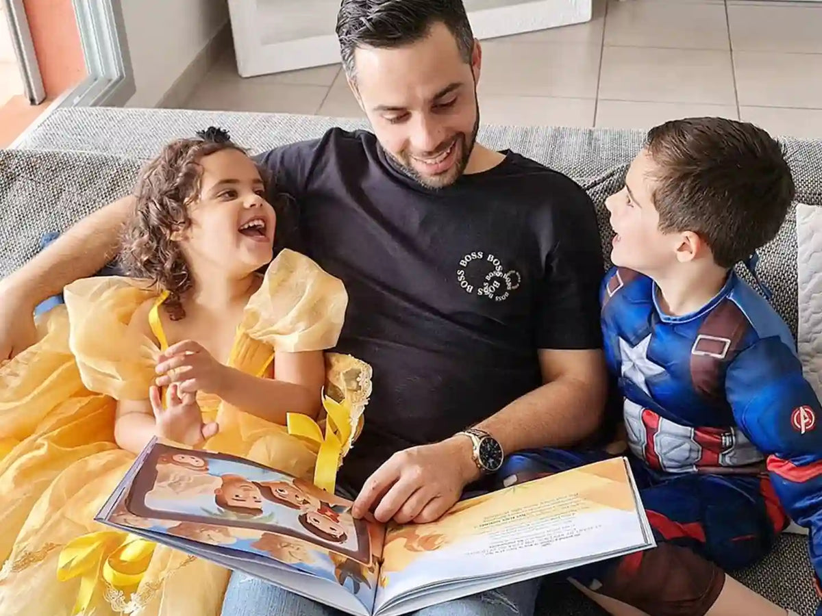 Die Kinder lachen ihren Vater an, der ihr personalisiertes Buch zum Vatertag liest.