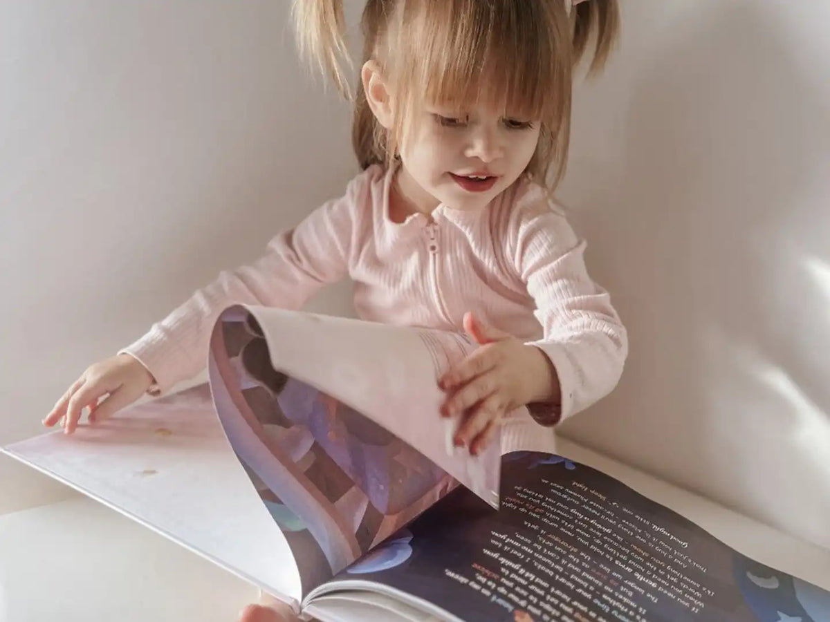 Kleines Mädchen blickt in ihr personalisiertes Bilderbuch, in dem sich ihre Mutter mit ihrem Kind die Zukunft vorstellt.