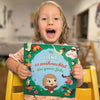 Kleines Mädchen lächelt und hält ihr personalisiertes Buch über Weihnachten in den Händen