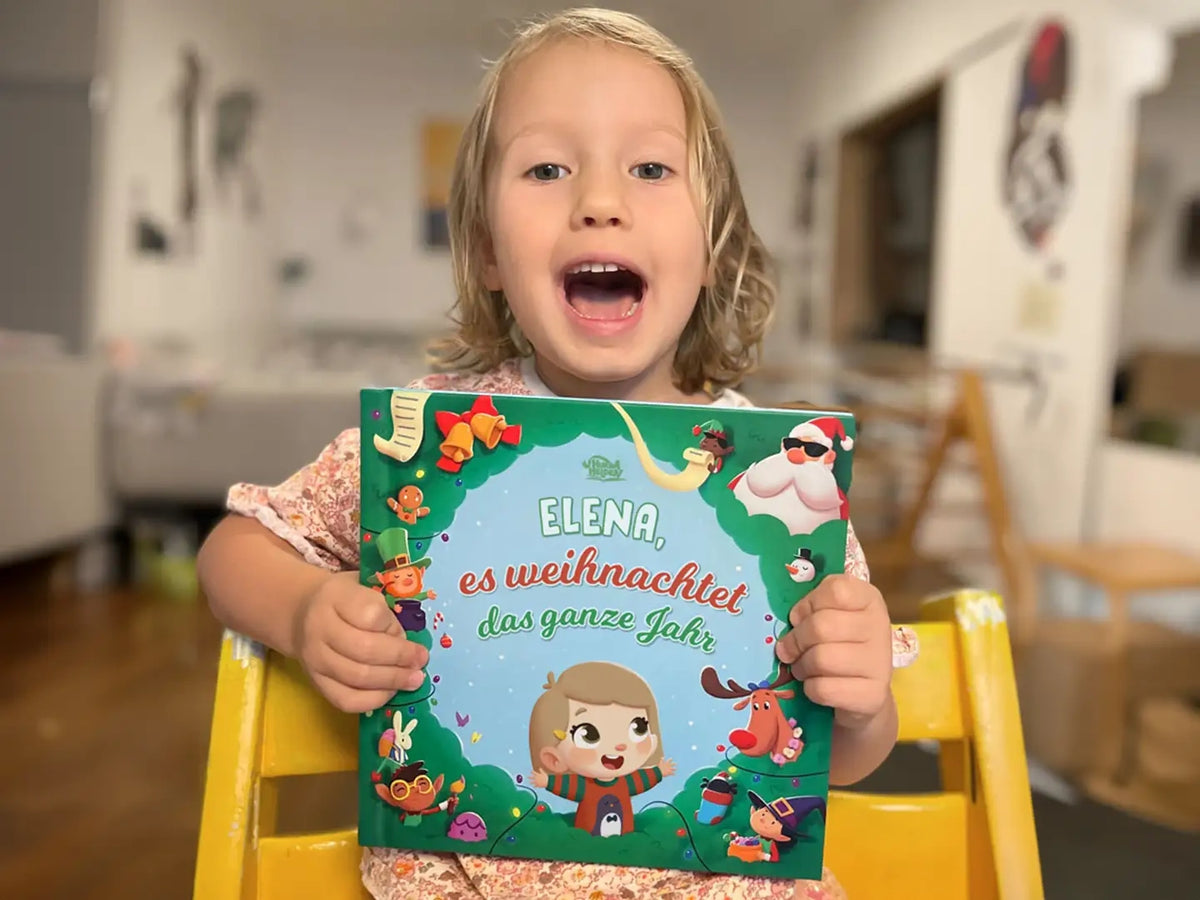 Kleines Mädchen lächelt und hält ihr personalisiertes Buch über Weihnachten in den Händen