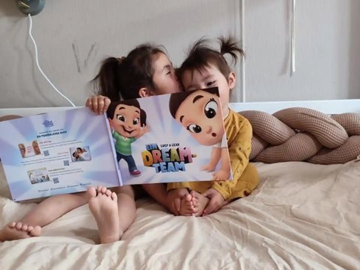 Eine große Schwester küsst ihre kleine Schwester, während sie ihr personalisiertes Buch von den Hurra Helden bestaunen. 