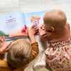 2 Kinder liegen auf dem Boden und blättern in ihrem personalisierten Buch für Geschwister von Hurra Helden. 