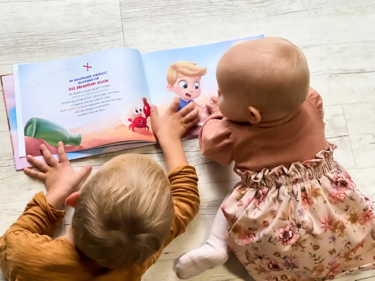 2 Kinder liegen auf dem Boden und blättern in ihrem personalisierten Buch für Geschwister von Hurra Helden. 