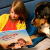 Ein kleines Mädchen lächelt über die Illustrationen ihres neuen personalisierten Buches, das nur für sie und ihren Hund  gemacht wurde.			