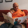 Ein Opa und Enkeltochter kuscheln auf der Couch und lesen im individuellen Buch von Hurra Helden. 
