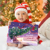 Baby im Weihnachtsoutfit hält das Buch „Leny & Mami – Erstes Weihnachten 2025“ auf einem Bett mit Tannenbaum im Hintergrund.