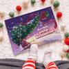 Blick auf das Buch „Nino & Mama – Erstes Weihnachten 2025“ mit Babyfüßen in Weihnachtssocken und Girlande im Hintergrund.