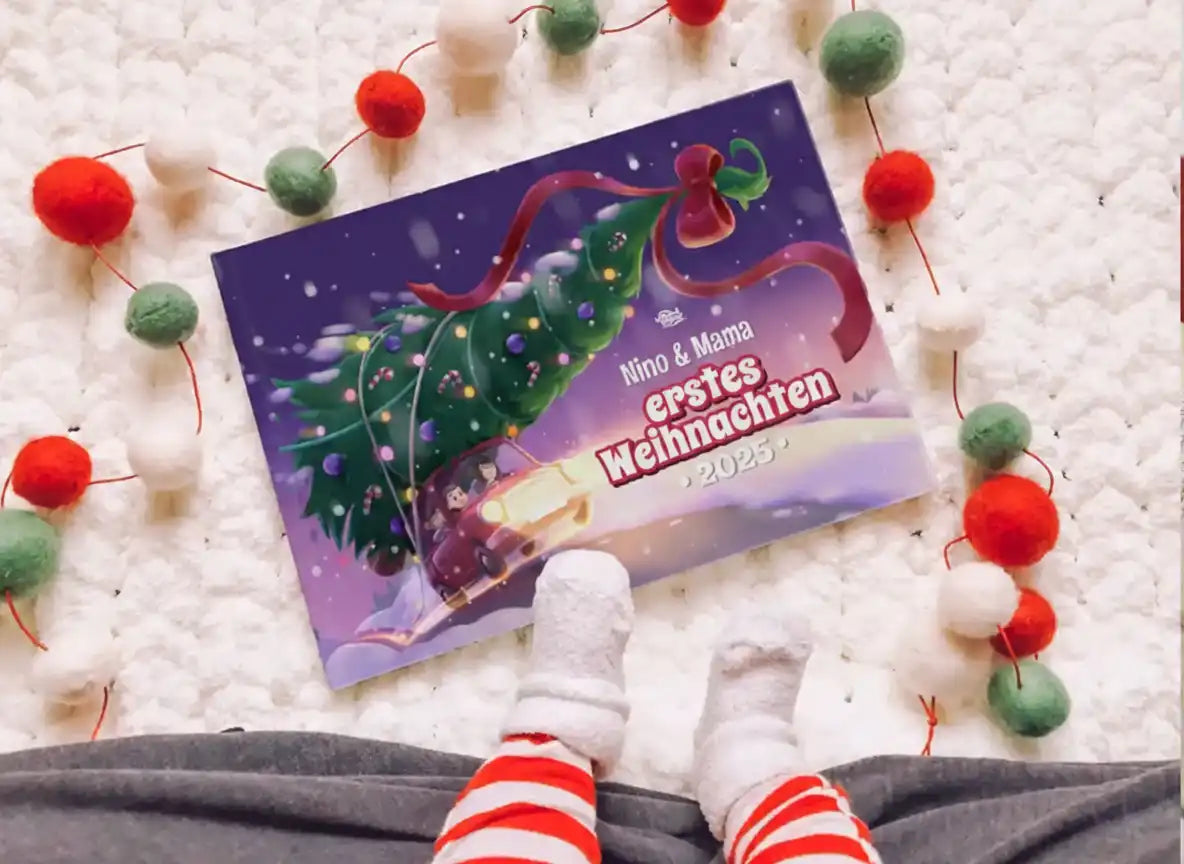 Blick auf das Buch „Nino & Mama – Erstes Weihnachten 2025“ mit Babyfüßen in Weihnachtssocken und Girlande im Hintergrund.