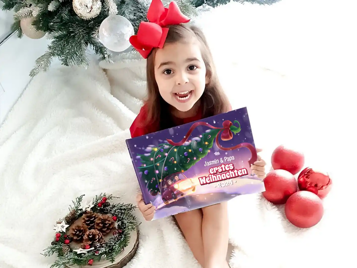 Kind sitzt vor einem Weihnachtsbaum und hält das personalisierte Buch „Jasmin & Papa – Erstes Weihnachten 2025“.