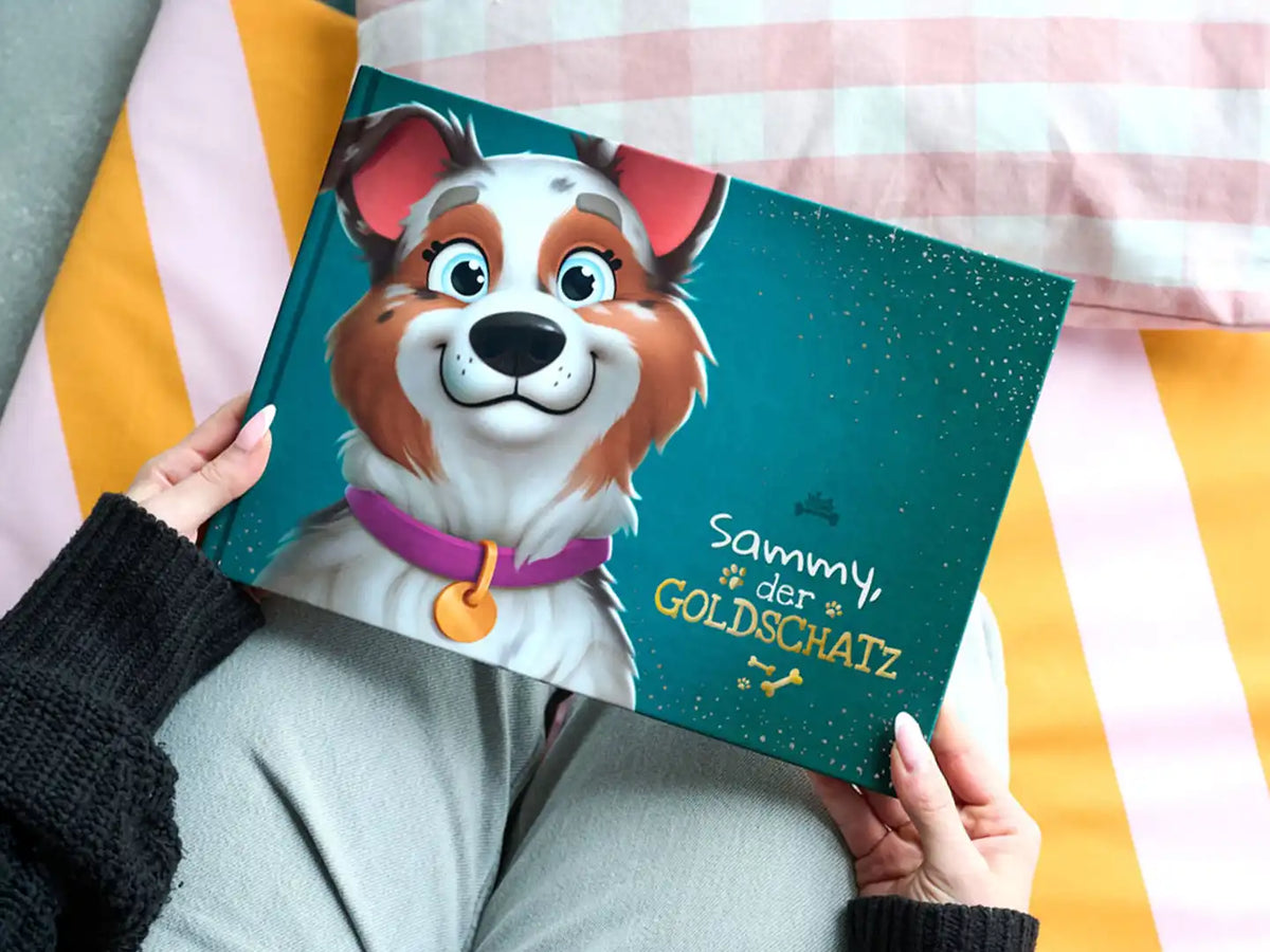 Person hält ein personalisiertes Premium-Hundebuch mit dem Titel „Sammy, der GOLDSCHATZ“ mit einem fröhlich gezeichneten Hund auf dem Cover.